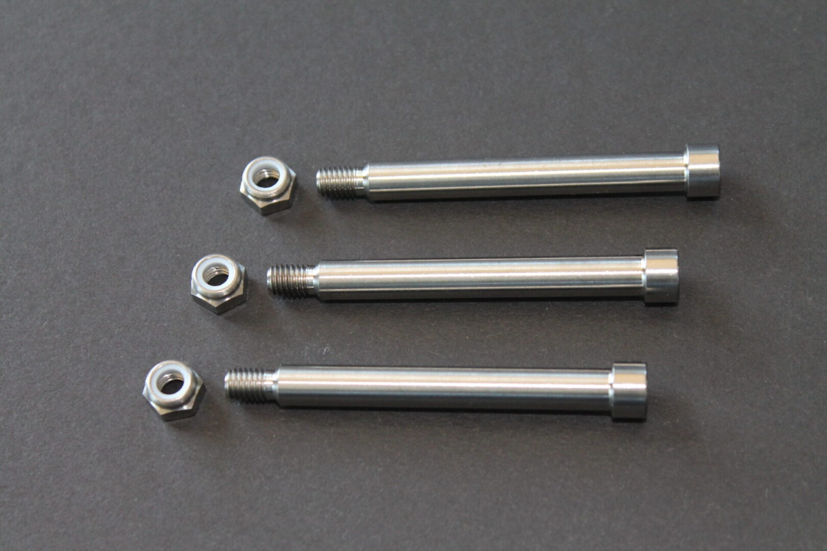 Four stainless steel bolts and nuts on a gray surface.
